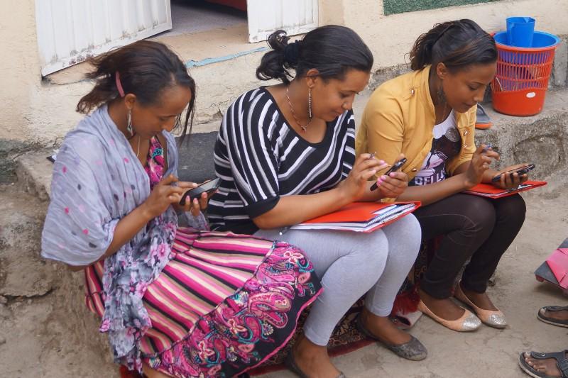 Three women setting on a step looking at cell phones